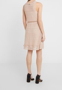 Robe en maille rose pâle avec un corsage ajusté, une jupe évasée, un motif texturé et un détail de bouton au dos au niveau de l'encolure.