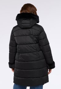 Schwarze wattierte Jacke mit Kapuze, ausgestattet mit einem samtigen schwarzen Kragen und Ärmeln. Das gestepptes Design hat horizontale Nähte und einen mittellangen Schnitt.