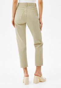 Ljusbeige högmidjade byxor med rak benpassform. Har två bakfickor och synlig sömnad. Tillsammans med ljusa klackskor.