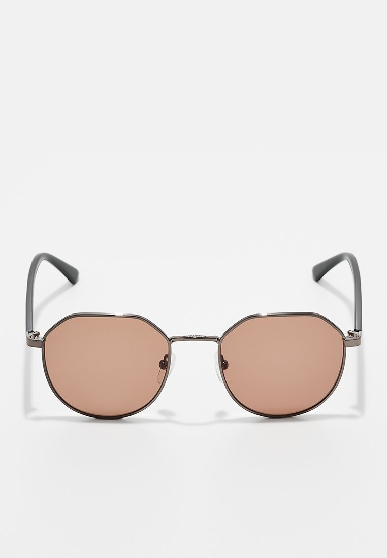 Occhiali da sole ottagonali con lenti marroni e sottili montature in metallo grigio scuro. Include braccia diritte standard con punte in gomma per il comfort.