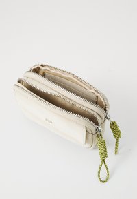 Portefeuille zippé crème en cuir texturé, doté de deux compartiments et de tirettes de fermeture éclair tressées vertes pour une manipulation facile.