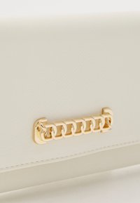 White textured handbag featuring a gold chain accent on the front, with a sleek, rectangular design and clean lines.