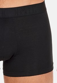 Black men's boxer briefs worn on waist and upper thighs, featuring a plain design with a wide elastic waistband.