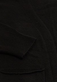 Schwarze Strickjacke mit weicher Textur, mit gerippten Bündchen und einer Tasche. Der Stoff wirkt dick und warm mit einem einfarbigen Design.