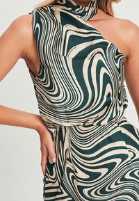 Vestido verde y crema con un diseño de un solo hombro, confeccionado en una tela suave que presenta líneas en espiral y un detalle de cuello alto.