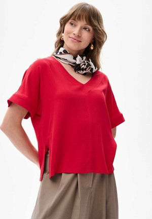 Rode V-hals blouse met korte mouwen en zijsplitten, gecombineerd met een zwart-wit gestippelde sjaal. Gladde stof, relaxte pasvorm.