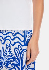 White cotton T-shirt with a visible brand logo, paired with a blue and white patterned skirt featuring abstract floral designs and wavy lines.