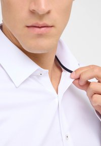 Witte button-down overhemd met een gestructureerde stof, voorzien van een contrasterende zwarte accenten onder de kraag en een open kraag die wordt aangepast.