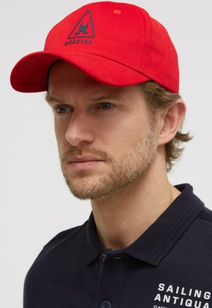 Man with short beard wearing red baseball cap with logo and navy blue polo shirt with white text "Sailing Antiqua."