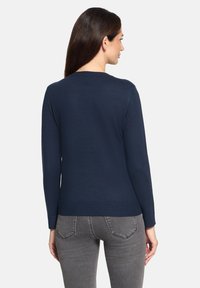 Pull bleu marine à col rond et manches longues, fabriqué dans un tissu doux. Ourlet et poignets côtelés, design minimaliste. Jean gris partiellement visible.