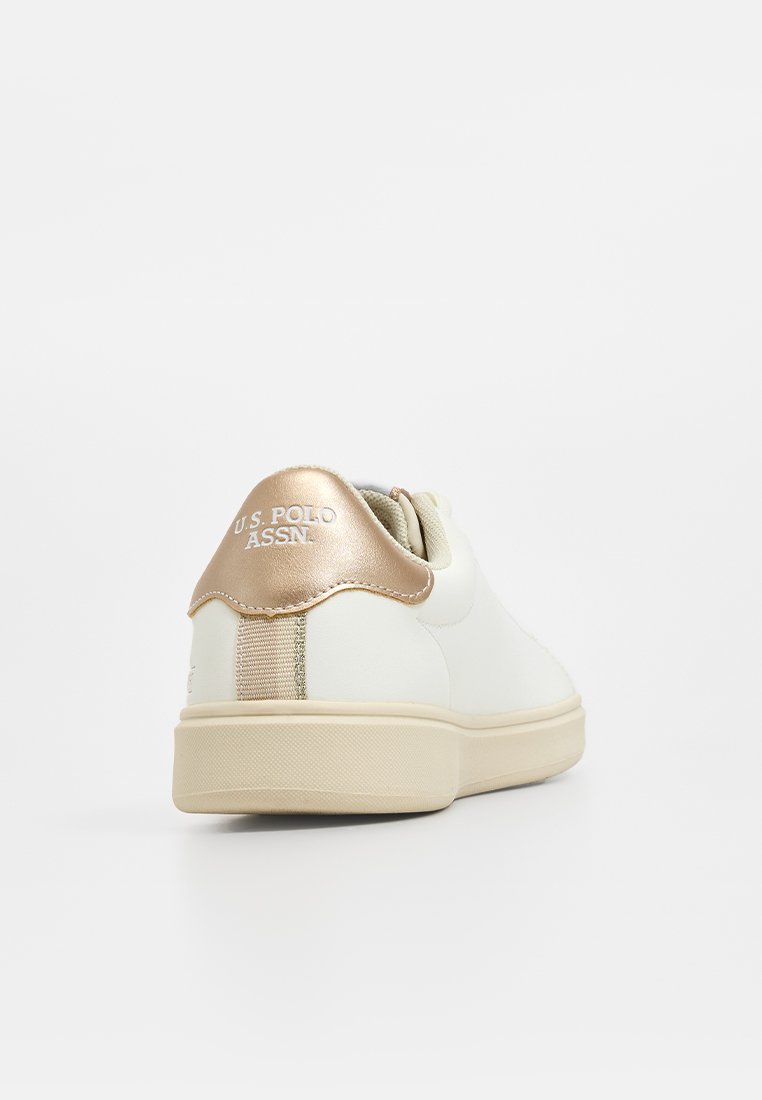 Baskets blanches avec une texture lisse, accent doré au niveau du talon arborant le logo U.S. Polo Assn., et une semelle en caoutchouc beige.