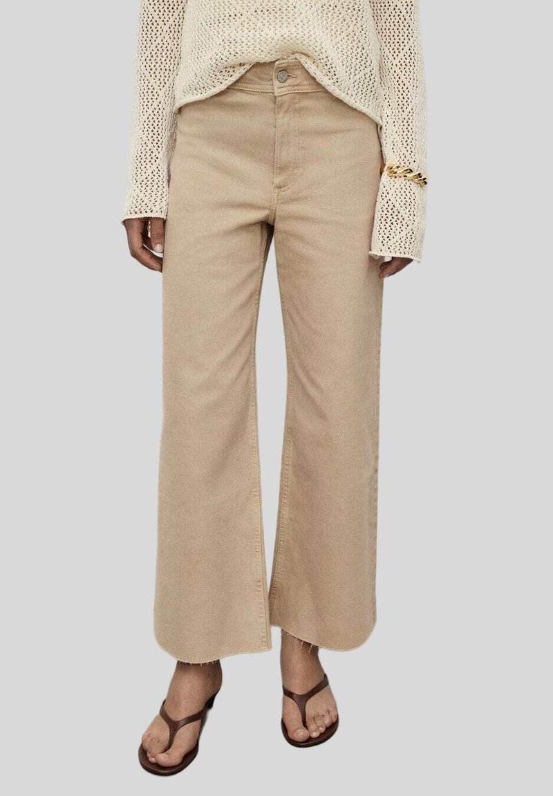 Beige wijde broek van katoen, met een hoge taille, een sluiting met een knoop aan de voorkant en rafelige zoomdetails, gestyled met een gebreide top en sandalen.