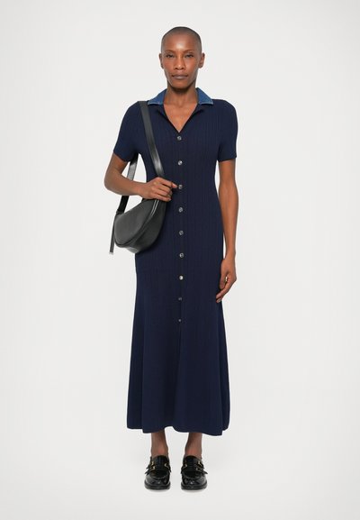 Marineblaues, geripptes Maxikleid mit kurzen Ärmeln, Knopfleiste und Denimkragen. Kombiniert mit einer schwarzen Umhängetasche und schwarzen Schuhen.