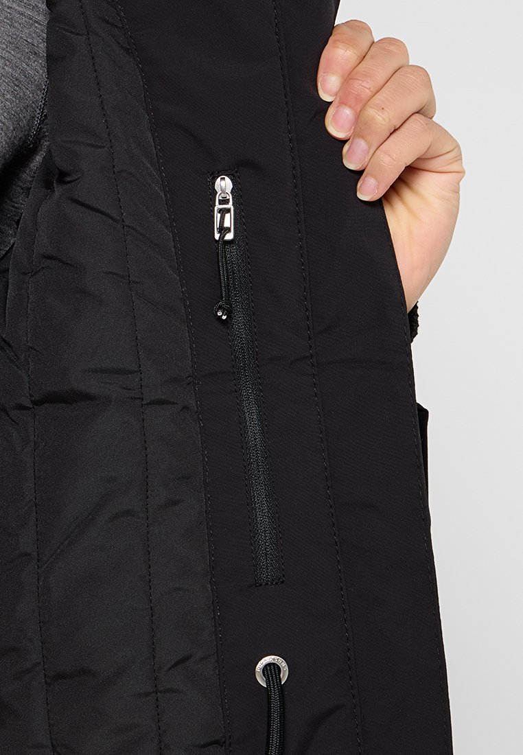 Schwarze isolierte Jacke mit einer Reißverschlusstasche und Kordelzug. Der Stoff hat eine strukturierte Oberfläche, die die Nähte und Designmerkmale hervorhebt.