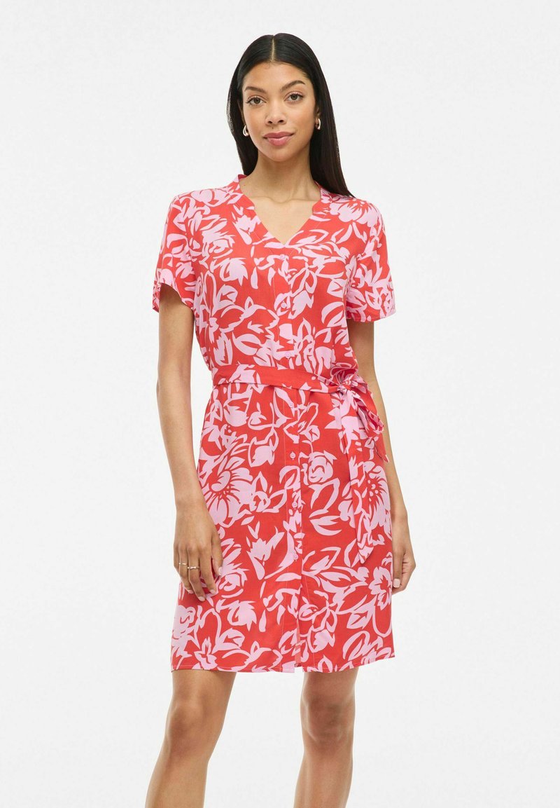Abito floreale rosso con maniche corte, scollo a V e dettaglio in vita con fiocco. Presenta motivi floreali astratti rosa su un tessuto leggero.