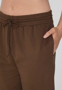 Braune Sporthose mit elastischem Bund, Kordelzug und Seitentasche. Weicher Stoff mit lockerer Passform und minimalen Designdetails.