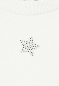 Biely textil s motívom hviezdy zo strieborných krištáľov, s textúrovaným rebrovaným výstrihom.