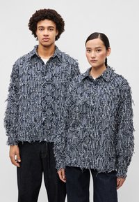 Tekstūrēti zili un balti svītraini žaketi ar saplēstiem maliem, ar pogu slēgšanu, brīvā piegriezumā un platām piedurknēm. Ikdienišķas denima bikses.