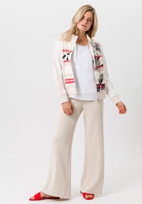 Lichtgewicht, gebloemde bomberjack met een gestreept ontwerp, gecombineerd met een witte top en beige wijde broek; rode sandalen.