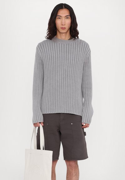 Gray ribbed knit sweater with a crew neckline, paired with dark brown shorts. Model holds a light beige tote bag.