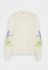 Witte linnen blouse met een knoopsluiting aan de voorkant. Bevat bloemapplicaties in blauw en groen op de mouwen. Pofmouwen met elastische manchetten.