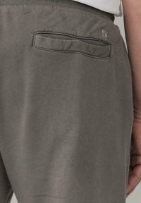 Grijze katoenen broek met een gladde textuur, voorzien van een achterzak en een klein logo-label op de tailleband. Elastische tailleband voor extra comfort.