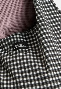 Zwart-wit geblokte stof met een zachte, roze, textuur binnenin. Inclusief een zwart label met het witte "ROXY" logo.