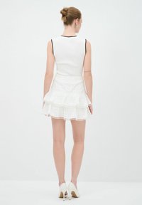 Haut sans manches blanc à manches côtelées avec des bordures noires, associé à une jupe blanche à plusieurs couches avec des accents en dentelle, complété par des chaussures à talons hauts blanches.