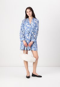 Rochie cu imprimeu floral albastru și alb, cu mâneci lungi și talie cu șnur, asortată cu o geantă albă și pantofi negri fără toc.
