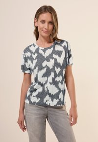 T-shirt en tricot à manches courtes présentant un motif abstrait gris et blanc, un col rond et une texture douce. Associé à un pantalon gris clair.