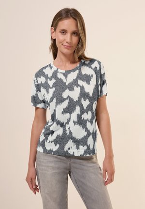 T-shirt en tricot à manches courtes présentant un motif abstrait gris et blanc, un col rond et une texture douce. Associé à un pantalon gris clair.