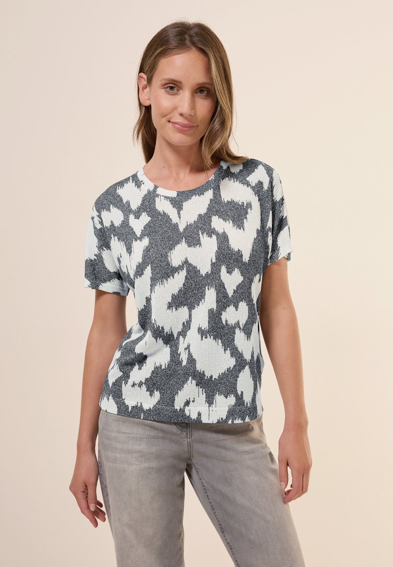 T-shirt en tricot à manches courtes présentant un motif abstrait gris et blanc, un col rond et une texture douce. Associé à un pantalon gris clair.