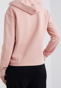 Sudadera con capucha rosa que presenta una textura suave, un corte casual y puños de canalé, combinada con pantalones negros. Enfocada en la simplicidad y la comodidad.