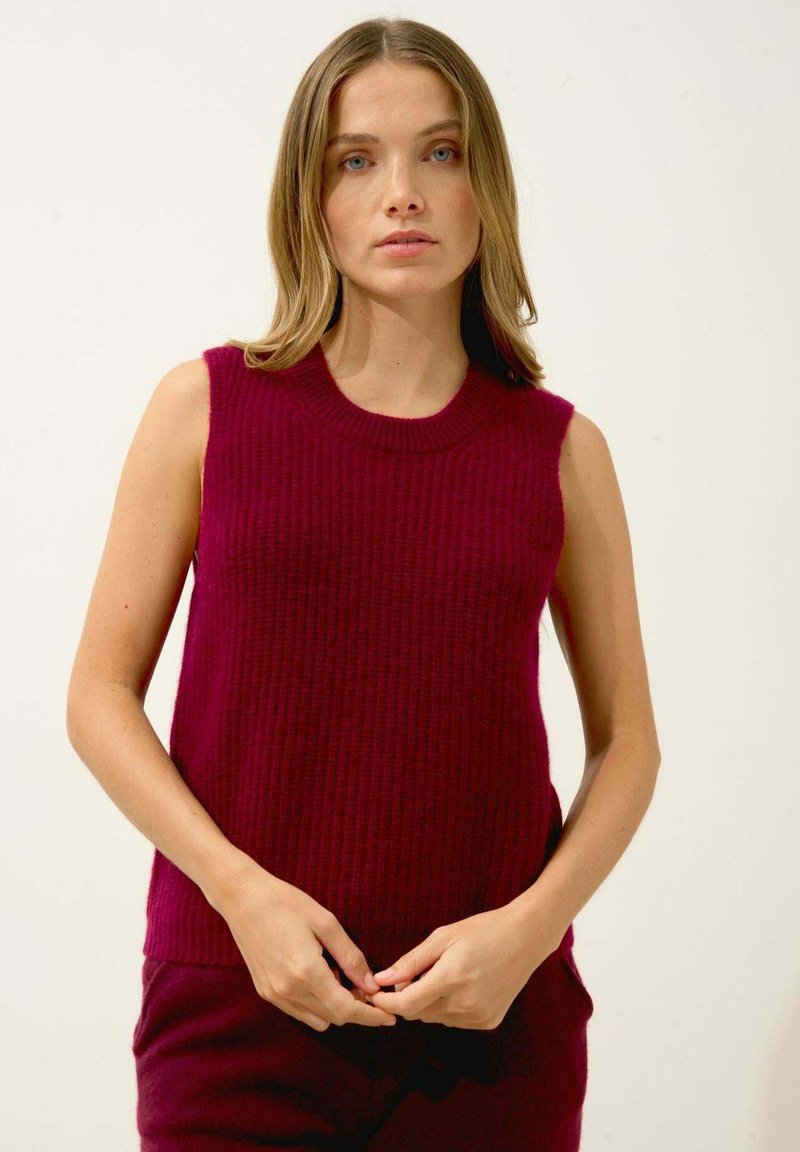 Burgundy ärmlös tröja med ribbat mönster och rund halsringning, bärs över matchande byxor, visad mot en vit bakgrund.