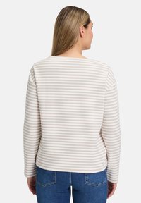 Hellbeige Pullover mit weißen horizontalen Streifen, runder Ausschnitt und langen Ärmeln, kombiniert mit blauen Jeans. Weiche Textur und schlichtes Design.