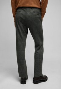 Donker geruite broek met een tailored fit, vervaardigd uit een gestructureerde stof, achterzakken en subtiele bruine accenten. G gedragen met zwarte schoenen.