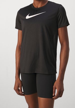 Personne portant un t-shirt noir à manches courtes Nike avec un logo blanc et un short noir ajusté, visible du cou jusqu’au milieu de la cuisse.