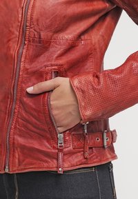 Red leather jacket featuring a zip closure, perforated sleeve accents, and adjustable side straps. Smooth texture with visible grain.