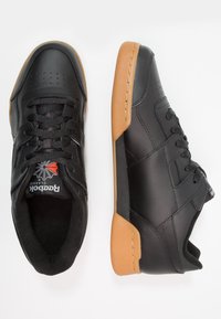 Svarte lær sneakers med gummisåle, med perforerte detaljer, flate lisser, og en rød og hvit logo på tungen.