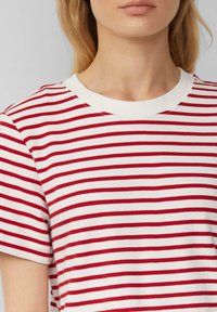 T-shirt à rayures rouges et blanches avec un col ras du cou et des manches courtes, fabriqué en tissu en coton doux, présentant des rayures horizontales uniformément espacées.