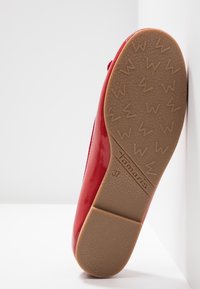Chaussure plate rouge avec semelle en caoutchouc texturée, marque "Tamaris" et taille 37 visibles sur la semelle, positionnée debout sur le talon.