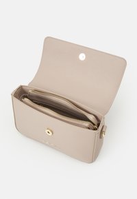 Béžová kožená přes rameno taška s klopou, zlatou kovovou ozdobou a několika vnitřními přihrádkami se zipovými detaily.