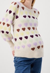 Pull de couleur crème avec un motif de petits cœurs texturés dans des tons de violet, vert, marron et jaune. Poignets et ourlet côtelés.