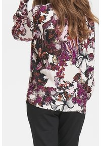 Blusa floral en tonos de rosa, púrpura y negro, con mangas largas y un tejido ligero y suave. Los patrones incluyen flores y mariposas.