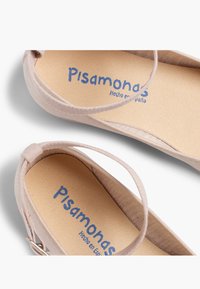 Light pink ballet flats with a soft fabric upper, featuring a thin strap and a beige insole with blue text, labeled "Pisamonas Hecho en España."