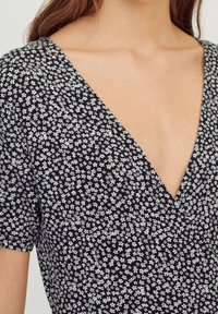 Vestido negro con estampado floral que presenta un profundo escote en V, mangas cortas y una tela ligera con pequeños patrones de flores blancas.