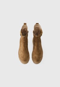 Botas de tobillo de ante marrón con punta redondeada, caña corta y cremallera lateral. Presentan un distintivo detalle de hebilla en tono dorado. Suela de goma.