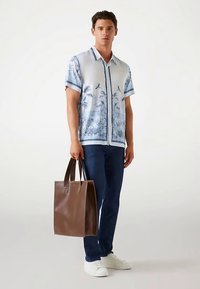 Korte mouwen blauw-wit overhemd met palmboomontwerp, gecombineerd met donkere jeans en een bruine leren handtas. Witte sneakers gedragen.