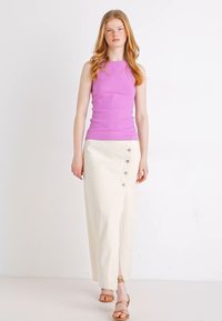 Haut sans manches violet clair associé à une jupe midi blanche avec des boutons sur le côté et une fente. Porté avec des sandales à lanières marron.