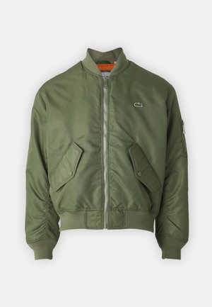 Jachetă bomber de culoare verde măslin, cu fermoar pe partea din față, manșete ribbed și două buzunare frontale. Prezintă un logo mic pe pieptul stâng și o captuseală interioară în contrast.